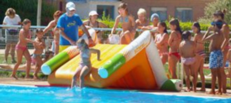 Varios niños disfrutan tirándose al agua desde un tobogán hinchable en la piscina municipal de La Albuera. / kamarero