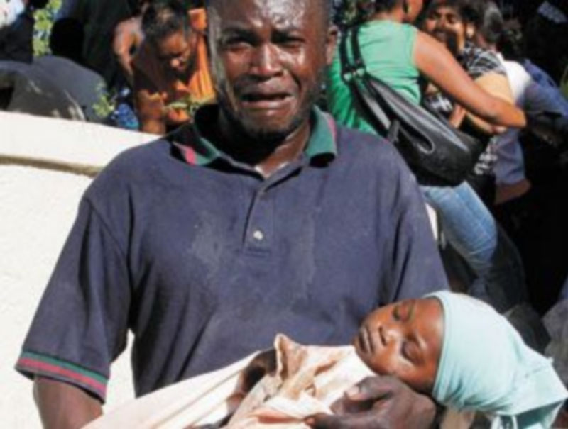 Un hombre herido lleva en brazos el cuerpo de su bebé muerto por una calle de Puerto Príncipe. / Eduardo Muñoz (Reuters)