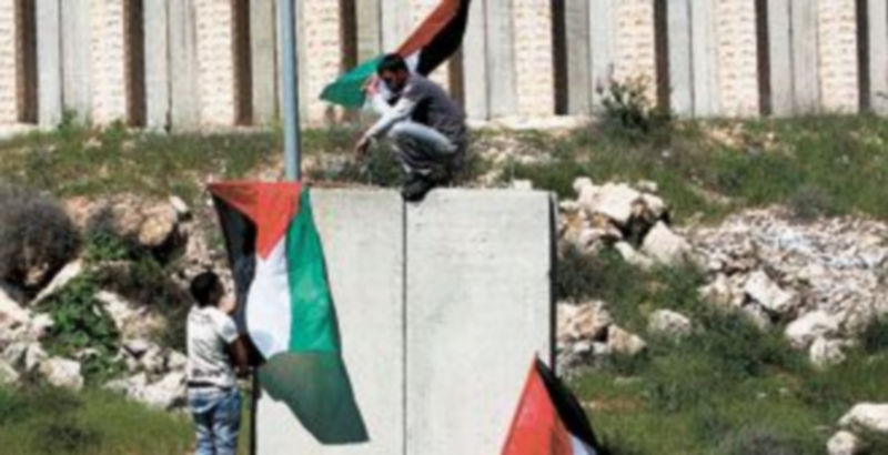 Tres jóvenes ondean banderas palestinas encaramados a una sección del muro de separación con Israel. / Efe