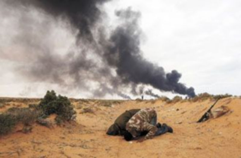 Miembros de las tropas rebeldes rezan en Ras Lanuf durante los bombardeos del Ejército de Muamar el Gadafi. / Goran Tomasevic (Reuters)