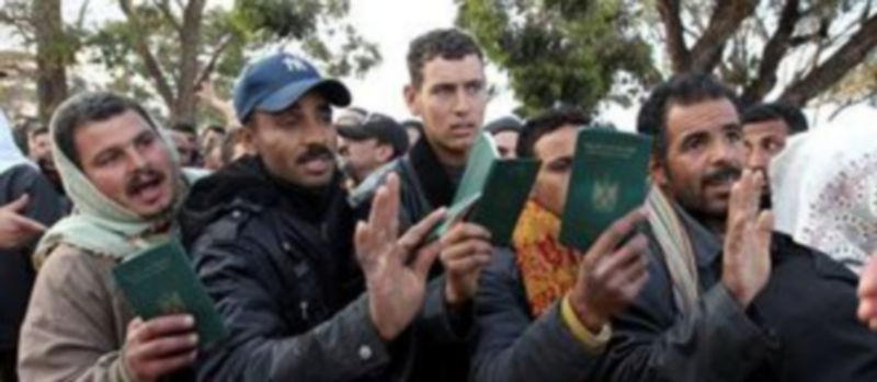 Refugiados egipcios provenientes de Libia muestran sus pasaportes mientras hacen cola ante un hospital militar de campaña en la frontera de Ras Jdir