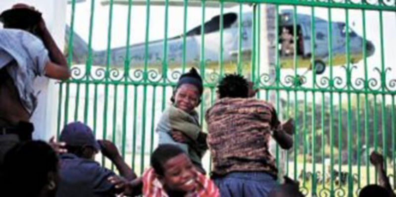Niños haitianos contemplan el aterrizaje de los helicópteros que ayer trasladaron a paracaidistas de EEUU al palacio presidencial de Puerto Príncipe. / C. Barría (reuters)