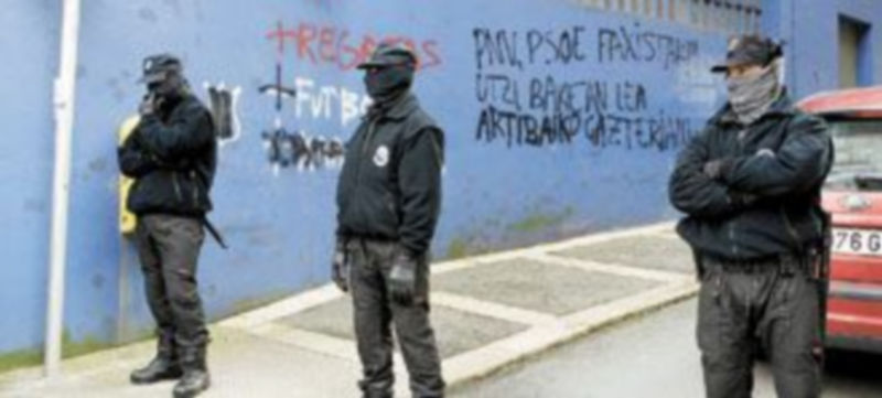 Varios miembros de la Policía autonómica vasca vigilan una calle para evitar que los vecinos de Ondarroa obstaculizaran los registros a los domicilios de los detenidos. / Efe