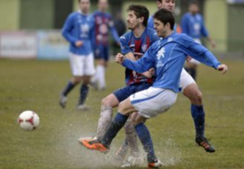 Dani Calleja y Laruso entran con fuerza a por la pelota en un momento del partido que estuvo marcado por la gran cantidad de agua que cayó sobre el terreno de juego. / Juan Martín