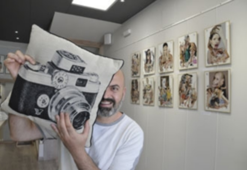Juan Carlos Monroy posa con un cojín con la imagen de una cámara junto a algunos de sus collages expuestos en la librería segoviana. / Juan Martín