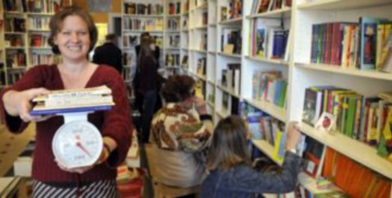 Una voluntaria de AIDA Books&More pesa varios libros mientras diversos clientes se interesan por las obras colocadas en las estanterías. / Juan Martín