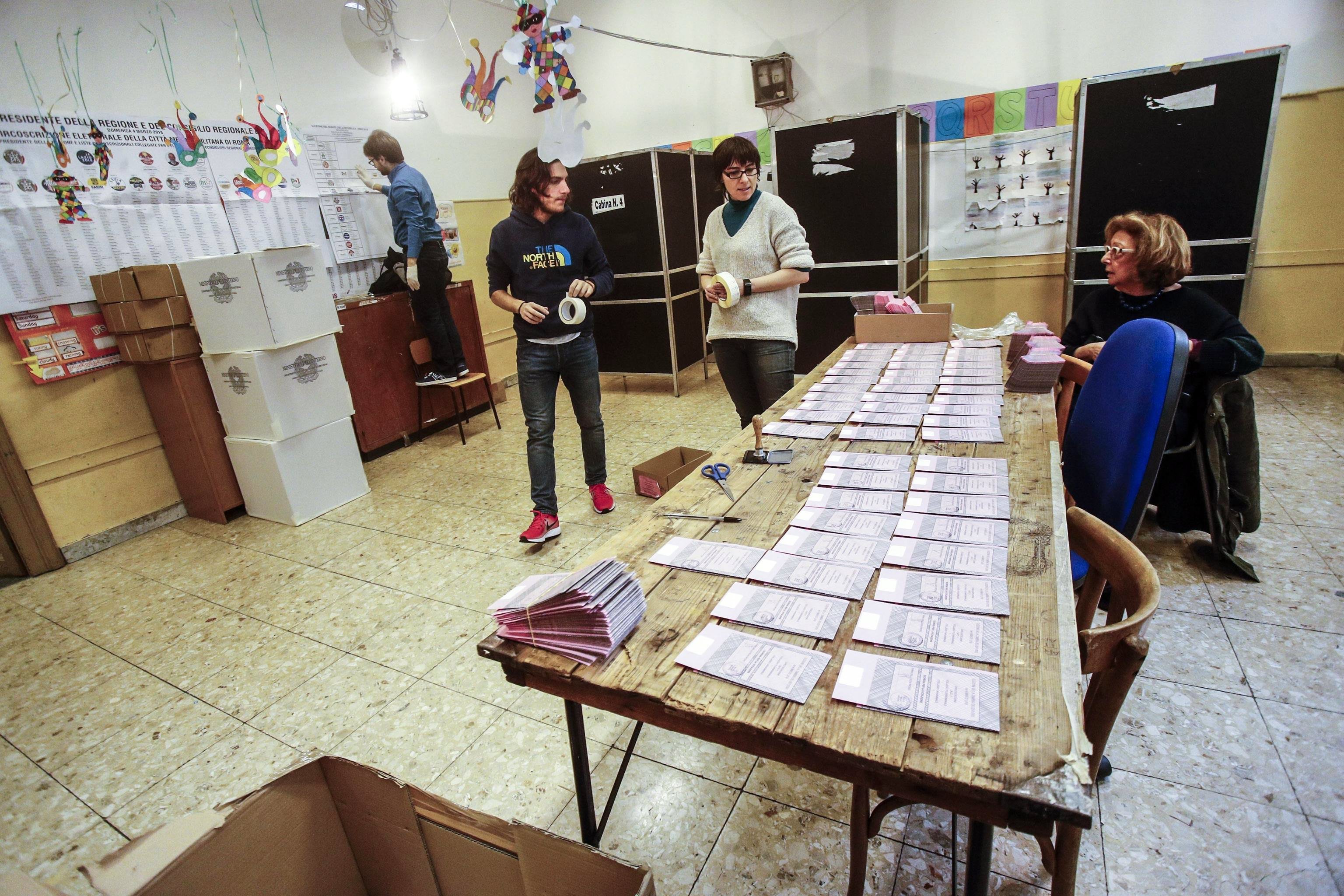 Varias personas preparan una mesa de votación para las elecciones que se celebrarán hoy en Italia. / EFE