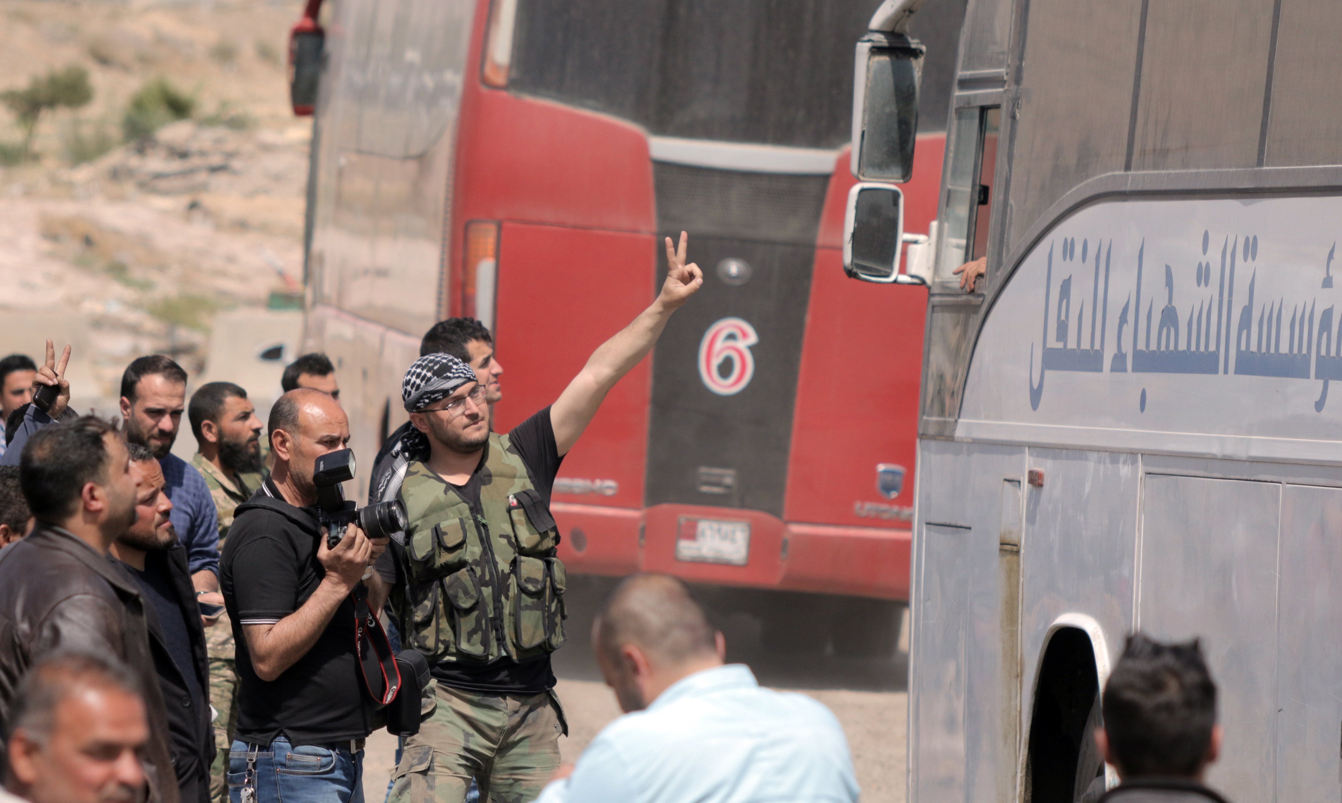Soldados sirios hacen el símbolo de la victoria frente a un autobús con miembros del Ejército del Islam, en Duma.