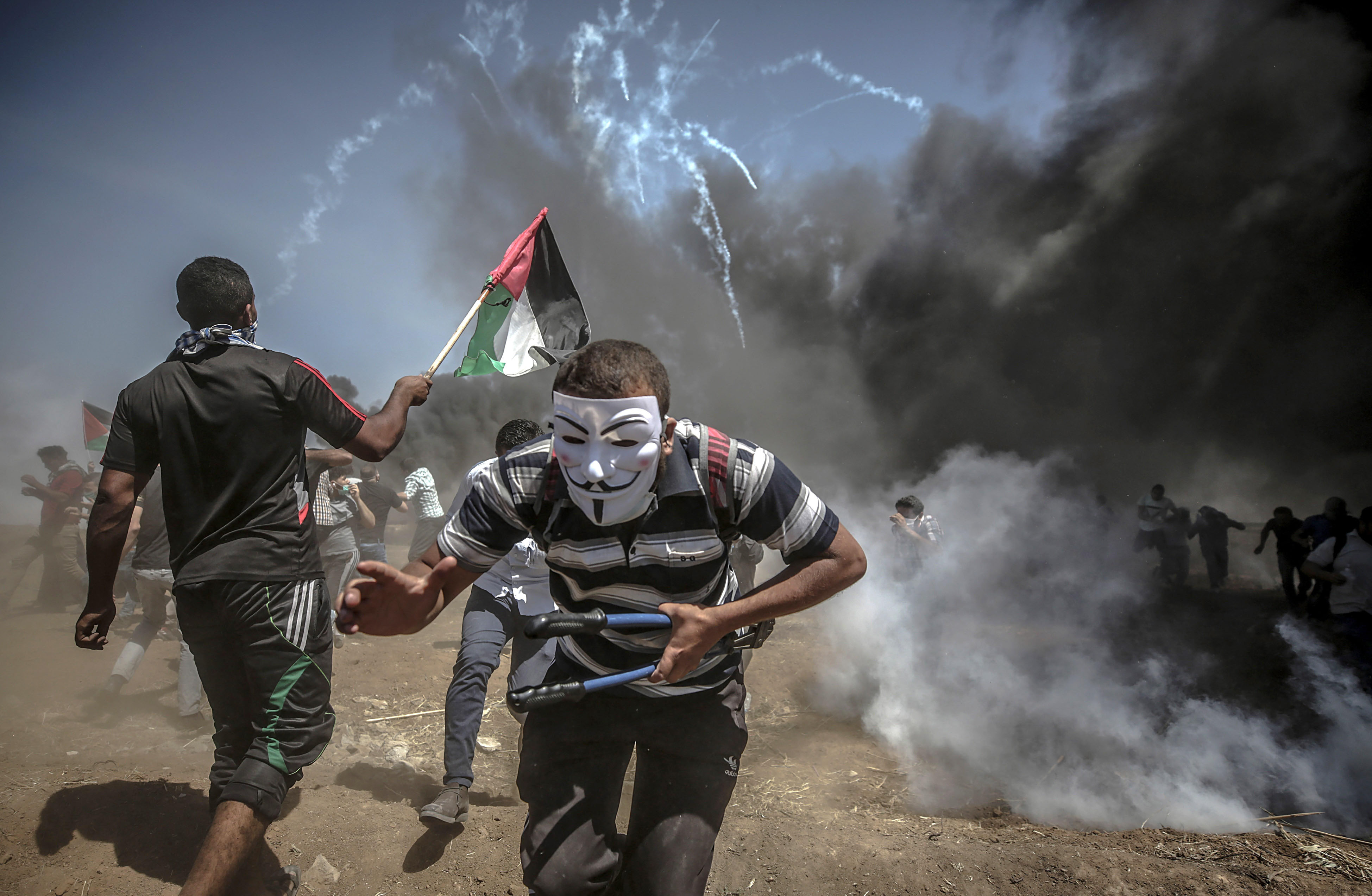 Manifestantes corren para protegerse del gas lacrimógeno lanzado por soldados israelíes en la frontera de Gaza.
