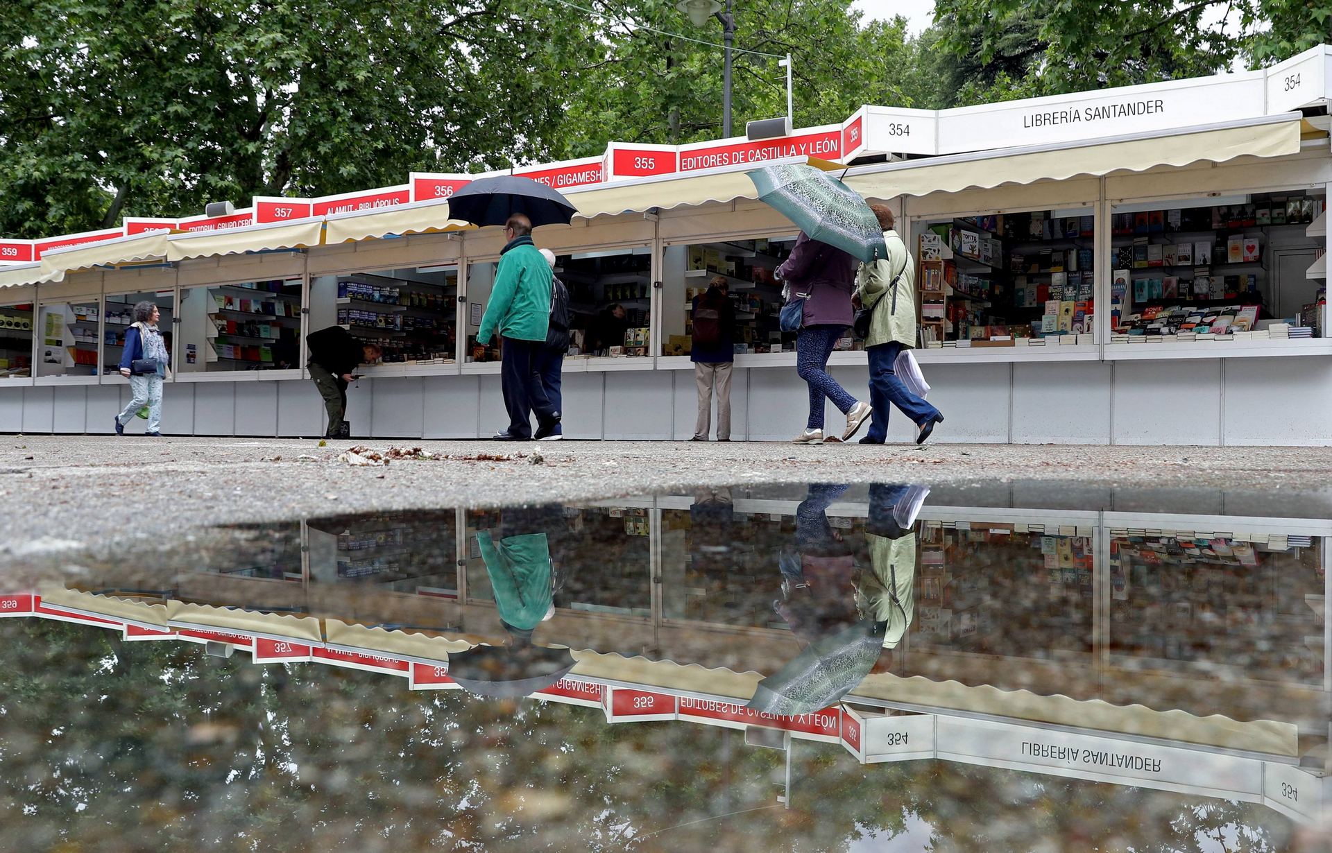 Algunos viandantes provistos de paraguas pasean y curiosean en las casetas instaladas en el Parque del Retiro con motivo de la 77 edición de la Feria del Libro de Madrid.