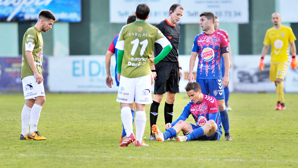El árbitro del partido conversa con Manu mientras Asier se baja la media esperando la llegada de la fisioterapeuta del equipo, tras la lesión que sufrió el centrocampista gimnástico. / KAMARERO