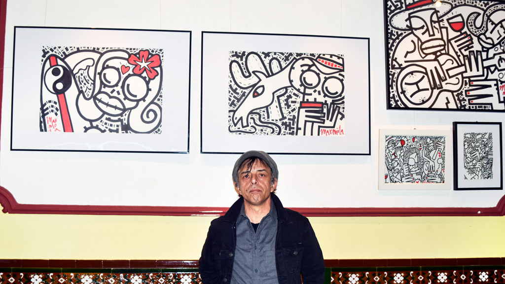 El artista arandino Toni Marmota, junto a varias de sus obras expuestas en el bar Santana de la capital segoviana.