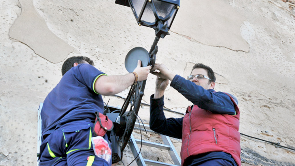 Dos operarios proceden a ubicar el dispositivo en el brazo de una farola. / Kamarero