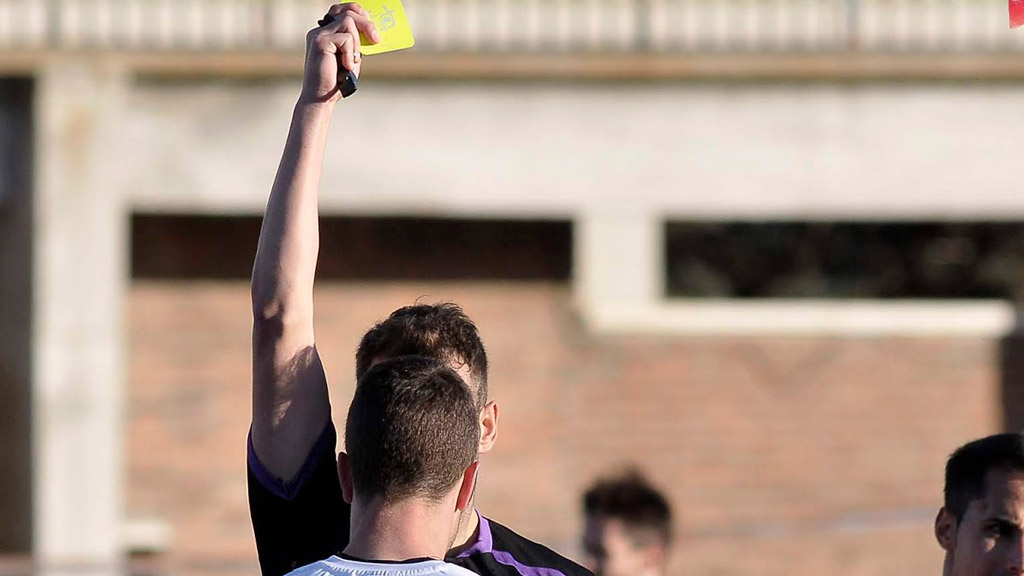 El árbitro del ‘Clásico’ frente al Ávila, muestra la tarjeta amarilla a Manu. / JUAN MARTÍN-GIMNÁSTICA SEGOVIANA