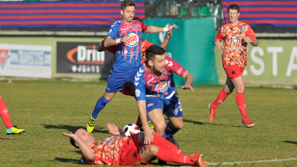 El atacante de la Gimnástica Segoviana Dani Calleja se dispone a tirar a puerta con el capitán del CD La Granja Diego Navarro ‘Pluma’ en el suelo. / KAMARERO