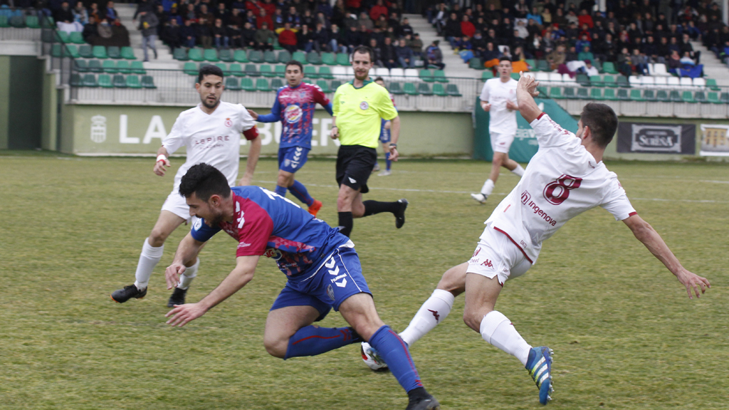 El delantero de la Gimnástica Segoviana Miguel Ángel Junco ‘Mika’ es derribado en una jugada frente a dos contrincantes del Júpiter Leonés. / NEREA LLORENTE