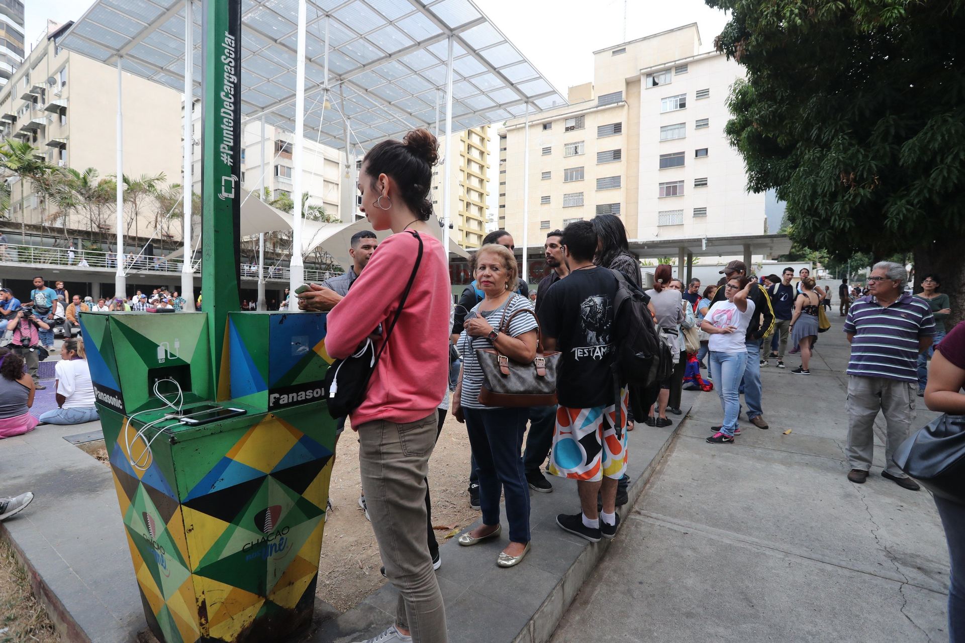 Varias personas hacen fila para recargar el móvil en un punto público durante el apagón eléctrico en Caracas.