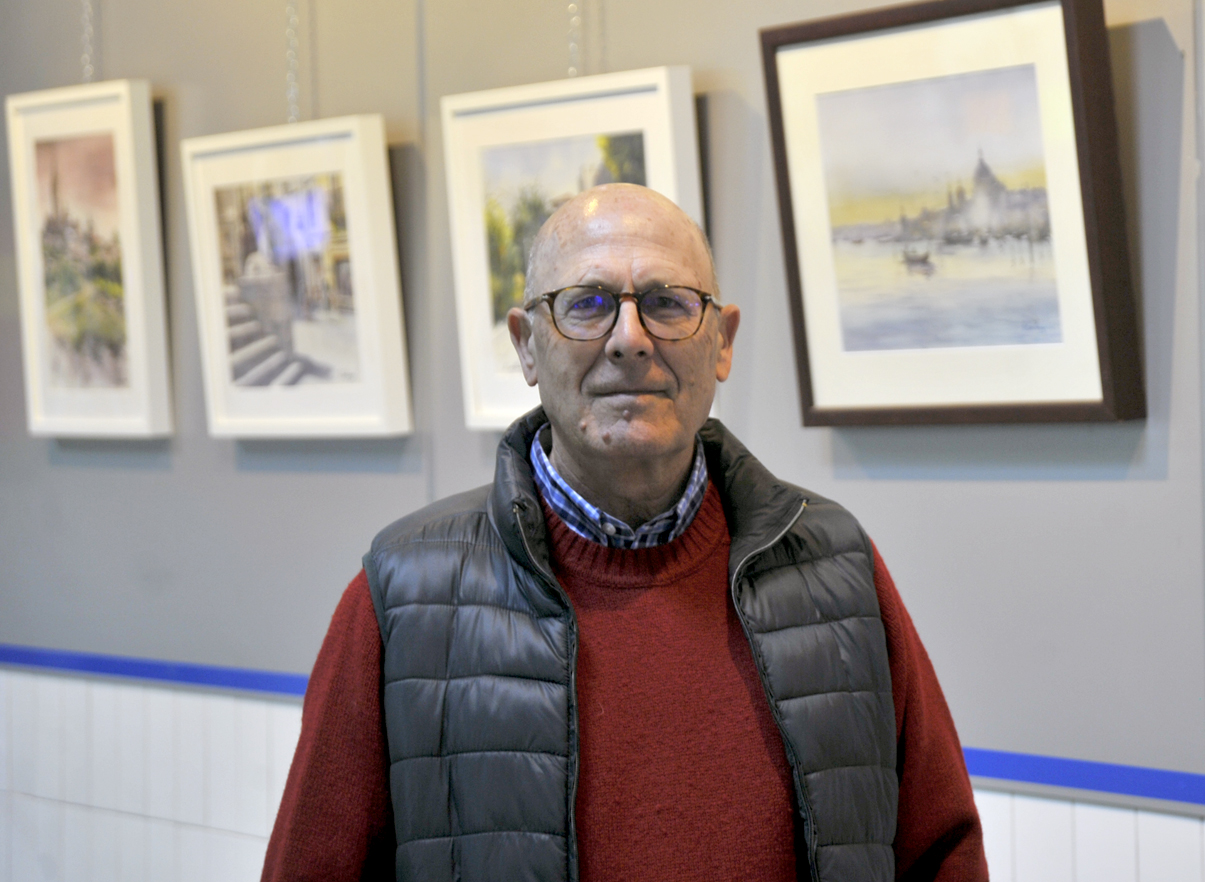 Sobre estas líneas, el acuarelista segoviano Ángel Contreras y varios visitantes admirando sus obras colgadas en los pasillos del Mercado Municipal de La Albuera.