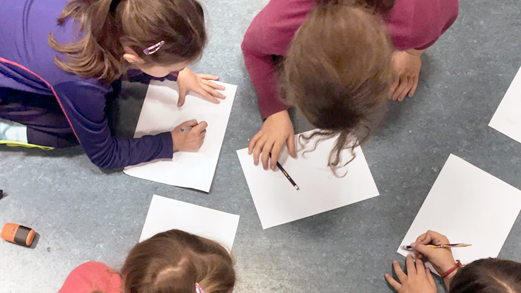 Un grupo de niñas escribe y pinta cuentos en el suelo del aula. / El Adelantado
