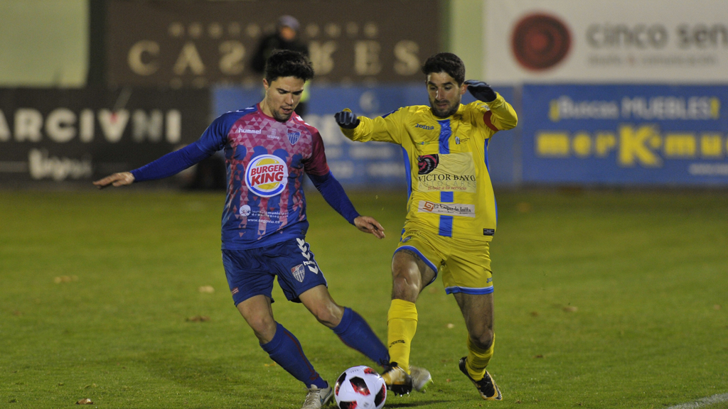 El jugador de la Segoviana Rubén se dispone a poner un balón en largo ante la presión del capitán de la Arandina, Ruba. / KAMARERO