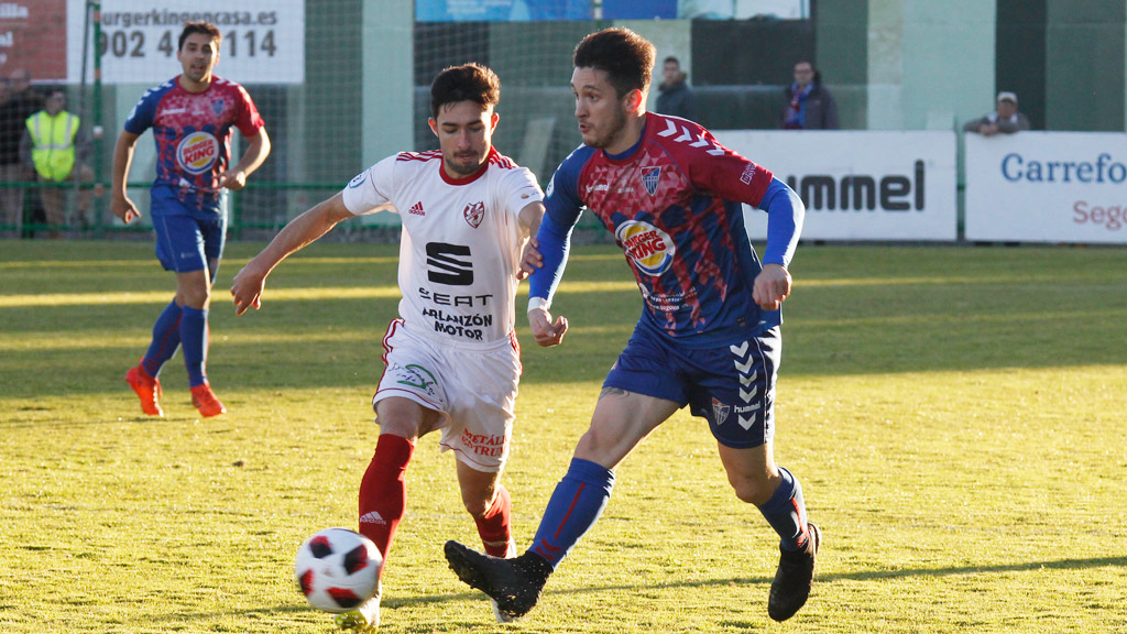 El lateral de la Segoviana Adrián Pérez pasa un balón ante la presión de un rival del CD Bupolsa. / NEREA LLORENTE