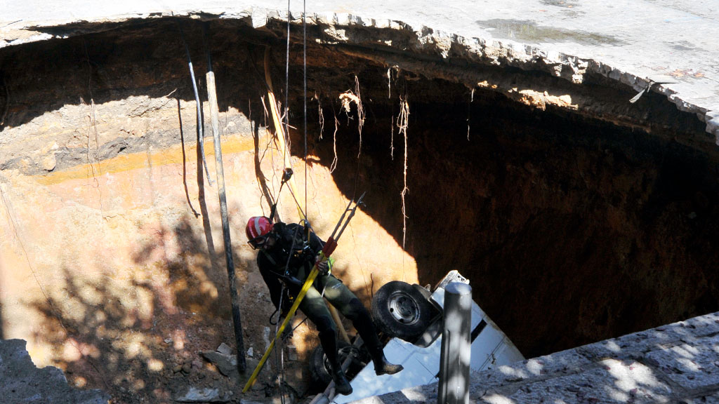 Un bombero desciende desde una grúa hasta el socavón para analizar el estado de la zona. / Kamarero