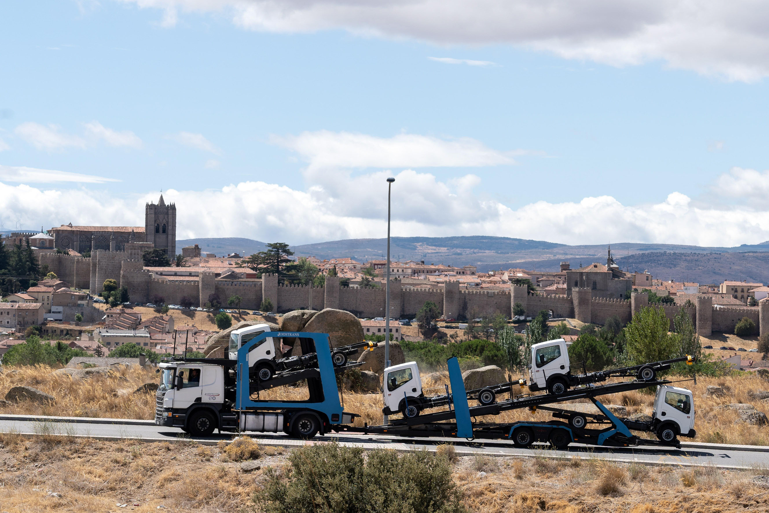 Varios camiones salen del Cylog de Ávila para su distribución, con la muralla al fondo. / EFE
