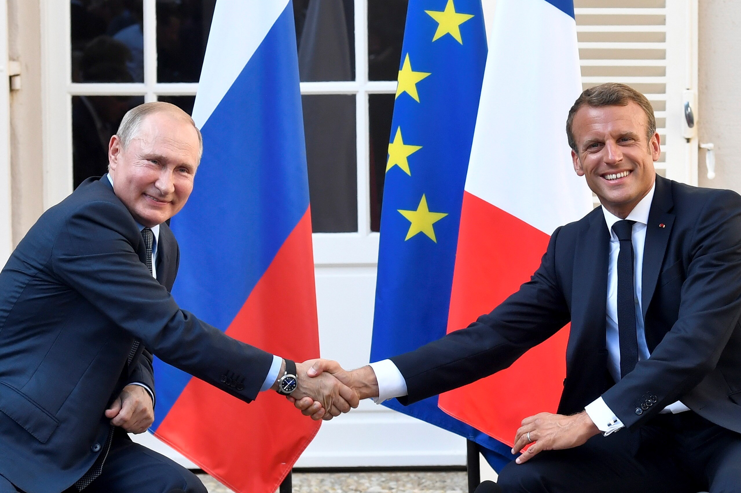Vladimir Putin (izq) y Emmanuel Macron se saludan ante las banderas de Rusia, Francia y la Unión Europea. / EFE