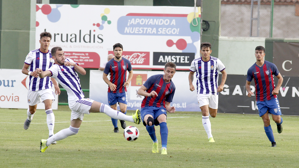 El jugador de la Gimnástica Segoviana Asier Arranz ejecuta un pase en el medio del campo y un contrincante del Real Valladolid B intenta cortarle. / NEREA LLORENTE