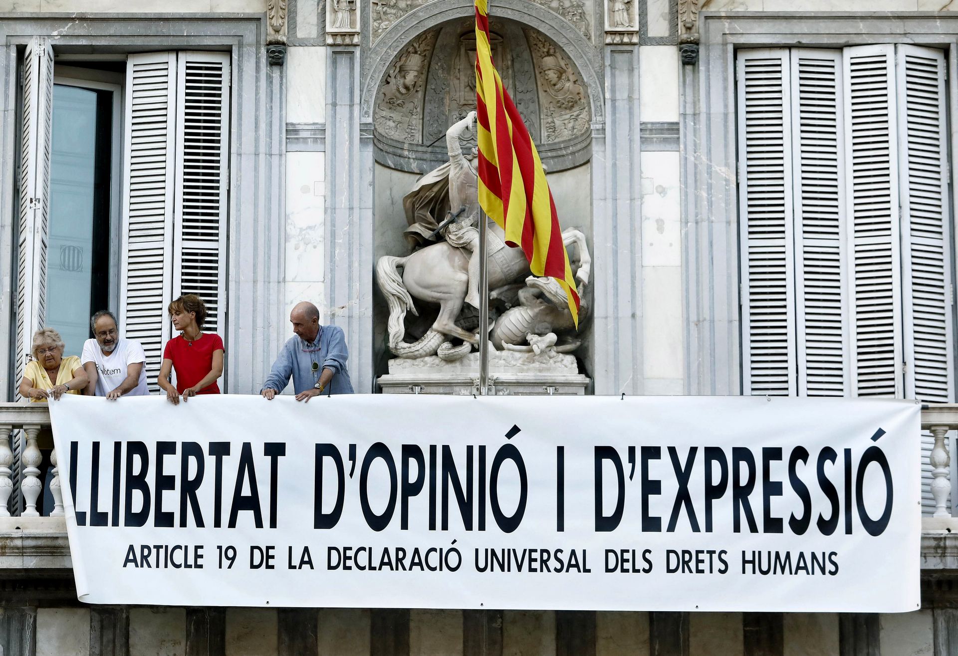 Dos exdiputados, una actriz y la portavoz de la plataforma Som Escola despliegan la nueva pancarta en la Generalitat. / EFE