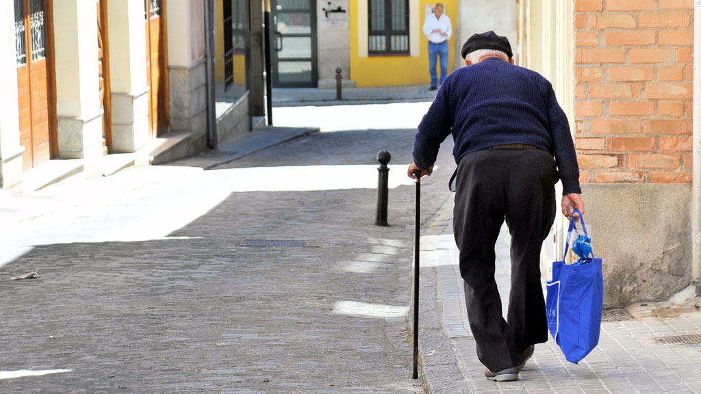 Un hombre mayor carga una bolsa de la compra por una calle de la capital segoviana. / KAMARERO