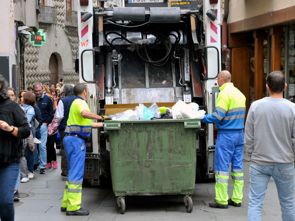 Trabajadores del servicio de limpieza preparan un contenedor para vaciarlo en el camión de basura. / Kamarero