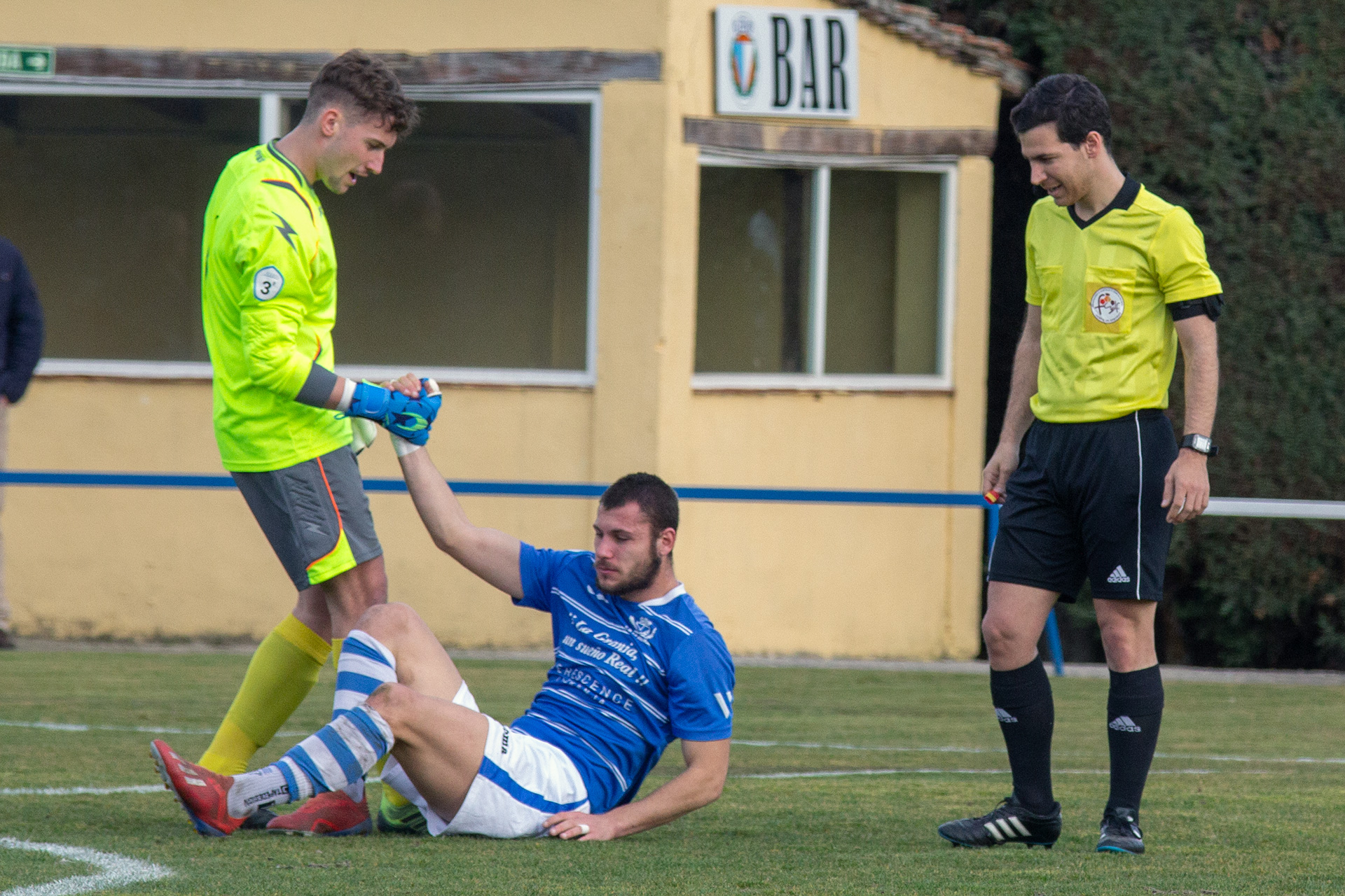 Un jugador del Real Burgos ayuda a levantarse al defensa del CD La Granja, Thanos./ NEREA LLORENTE