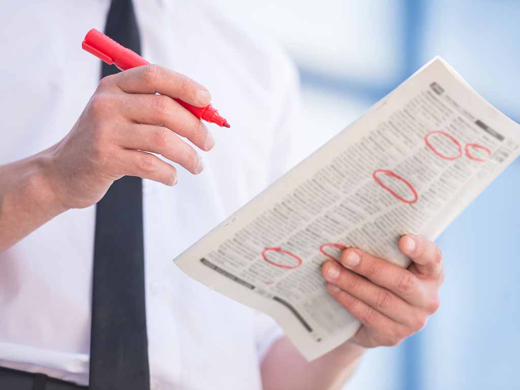 Close-up of unemployed man in suit reading newpaper outdoors.