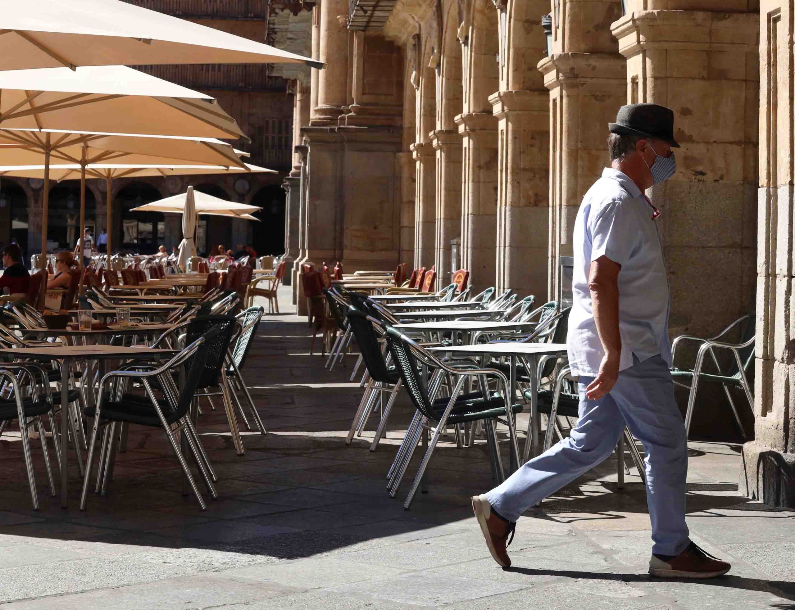 Un hombre con mascarilla pasa frente a una terraza de un restaurante de la plaza mayor de Salamanca. EFE/ J.M.GARCÍA