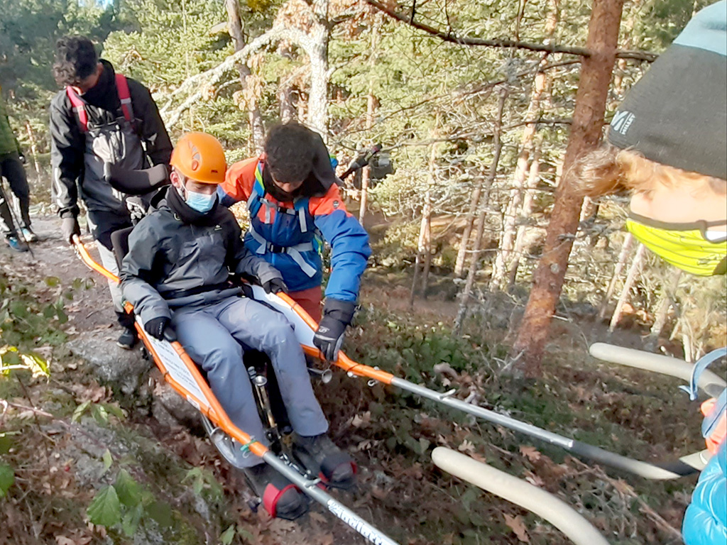 Tres alumnos portan a un cuarto sobre una silla joelette. / E.A.