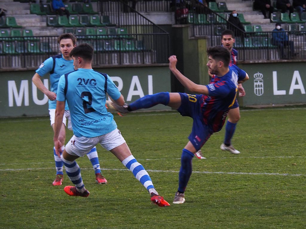 Dani Calleja golpea el esférico ante el intento de defensa de Cuadri en el gol del empate de la Segoviana durante el duelo disputado ayer La Albuera. / KAMARERO