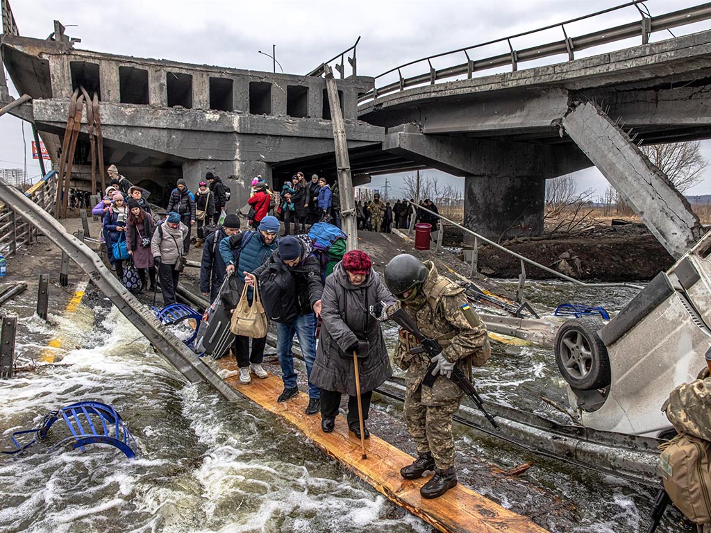 Civiles cruzan un puente destruido mientras huyen del asedio en la ciudad de Irpin, a unos 20 km de la capital, en Ucrania. / EFE - ROMAN PILIPEY