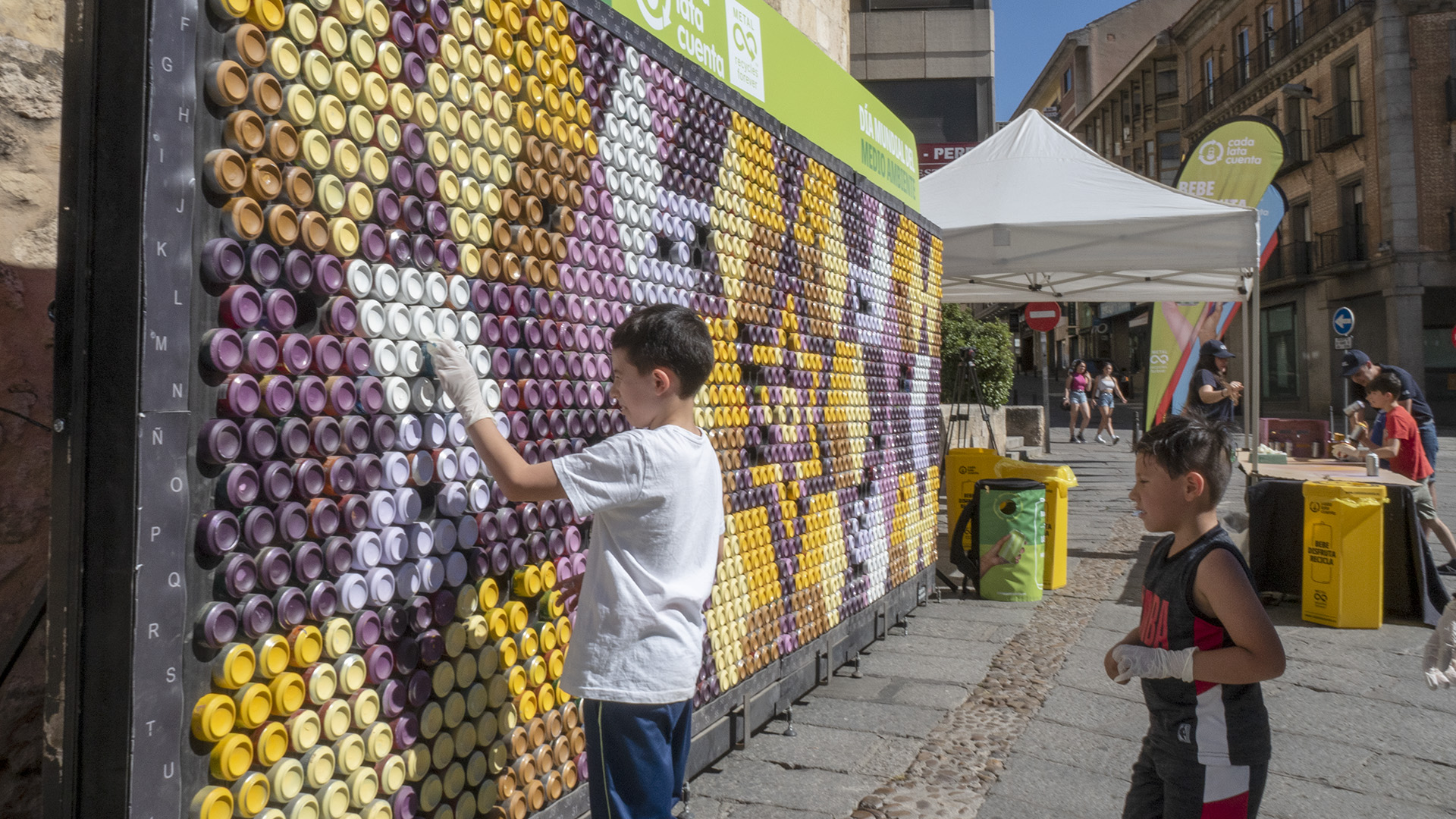 Dos niños participaban ayer por la tarde en la finalización de la pixelata o mural artístico realizado con latas en la avenida del Acueducto. / Nerea Llorente