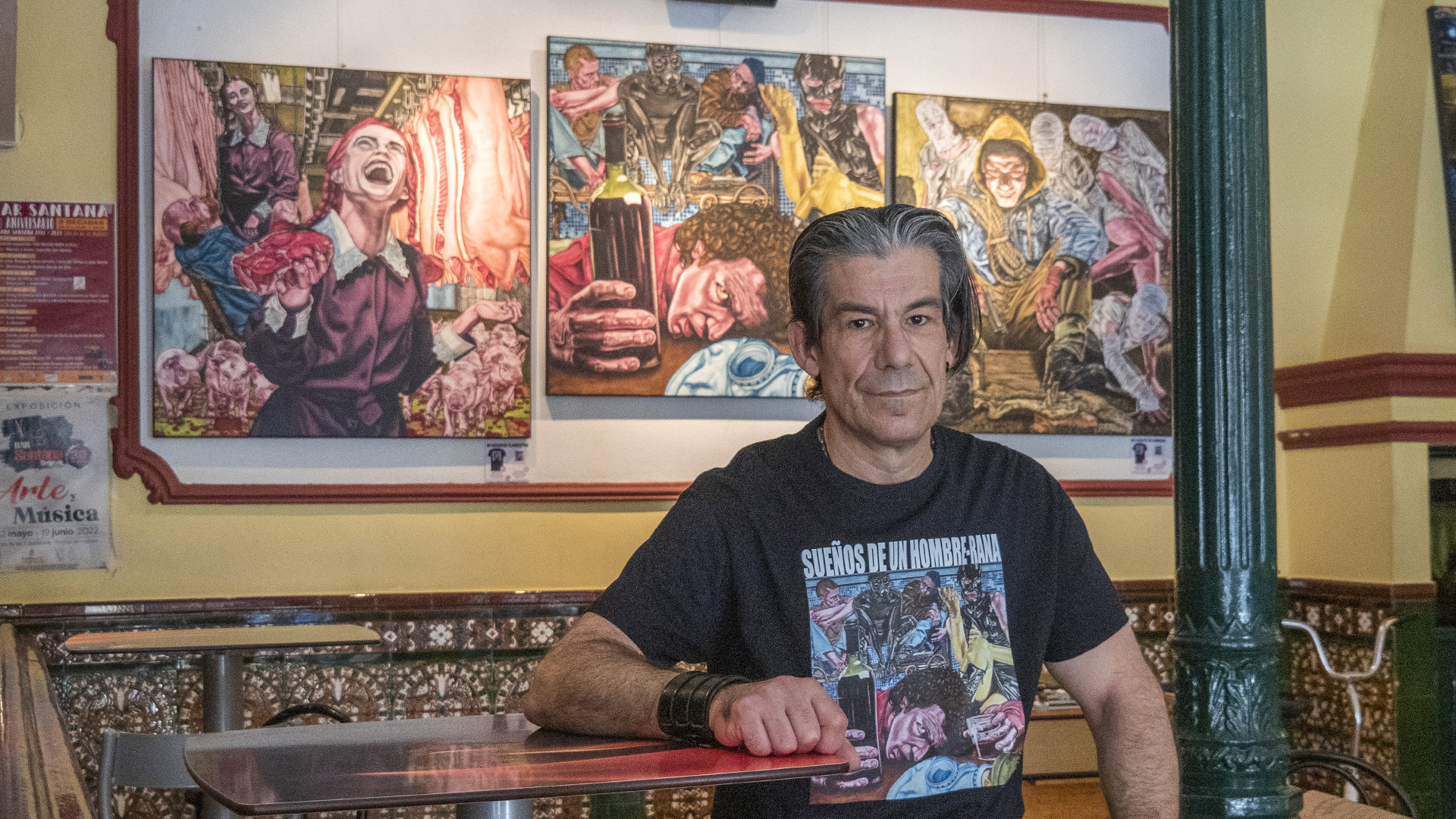 El pintor Fernando Ortega posa frente a tres cuadros de su última colección, ‘Seres en la Encrucijada’, disponible en el Bar Santana.