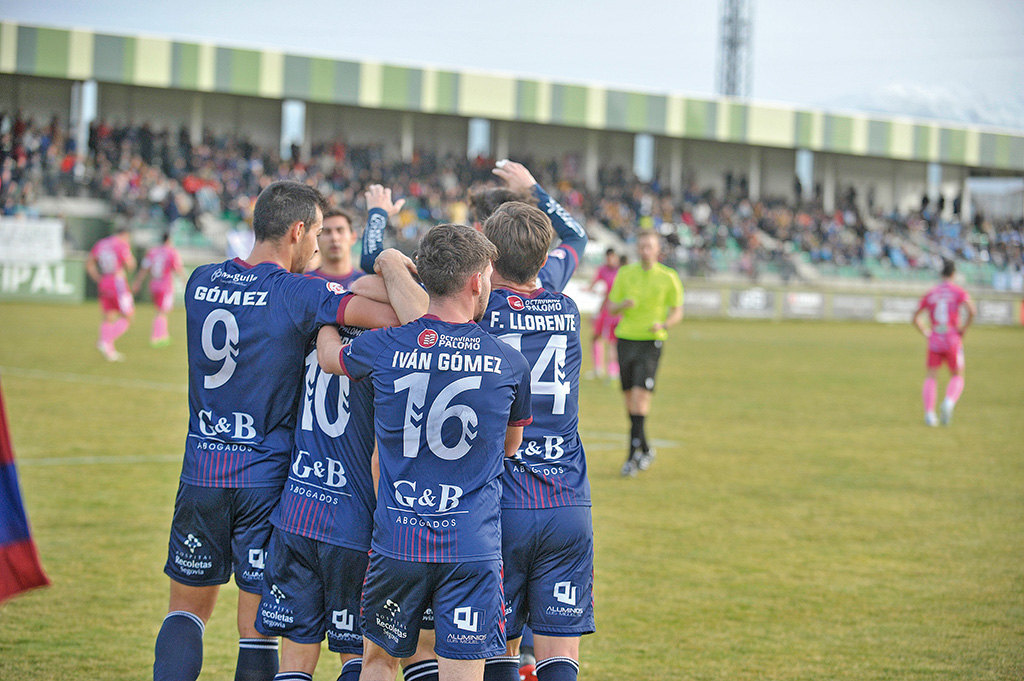 Los jugadores de la Segoviana celebran el primer tanto conseguido ante el Coria, con la grada llena de La Albuera al fondo./ KAMARERO