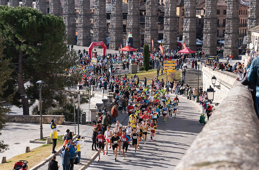 El millar de corredores que tomaron la salida en el Azoguejo inicia su paso por el Paseo Santo Domingo tras pasar por debajo del Acueducto./ MIGUEL ÁNGEL FERNÁNDEZ