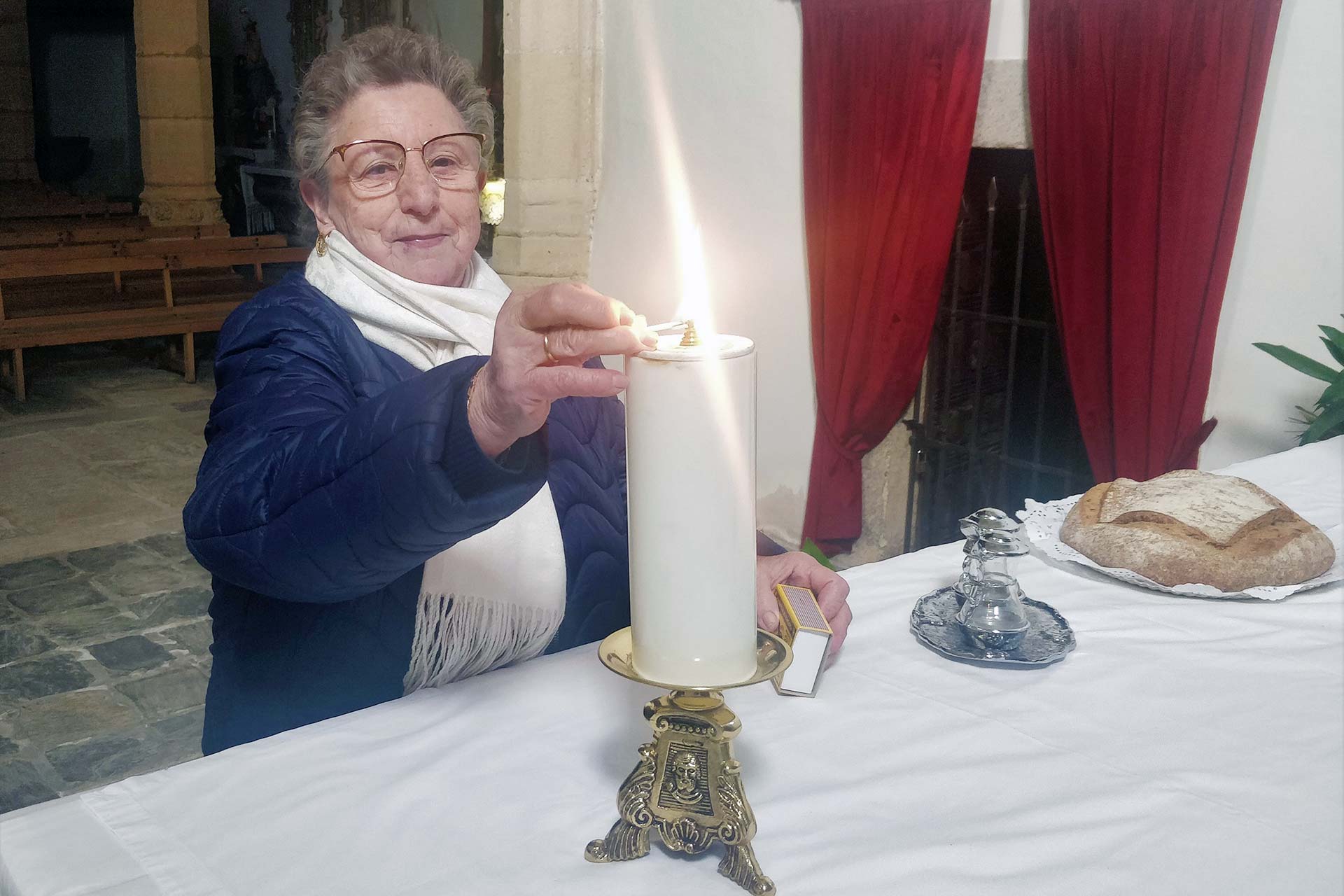 María Henar Olombrada, la sacristana de la iglesia de El Salvador, en Fuentepelayo, enciende un cirio en el templo. / Juan Cruz Serrano