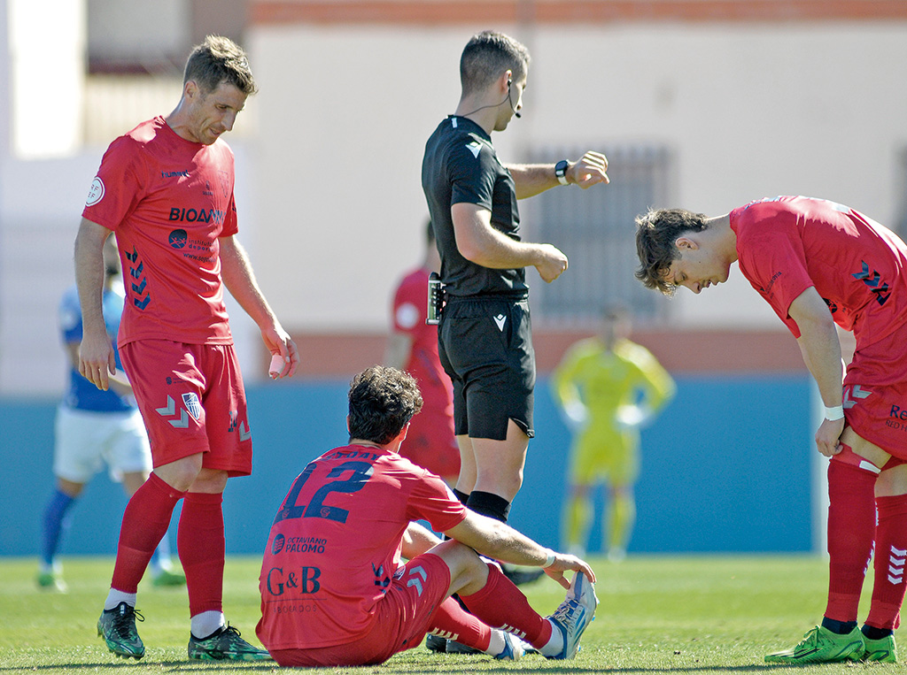 Plomer y Fer Llorente esperan la llegada de la fisioterapeuta de la Segoviana para atender a Pedro Astray, sentado en el suelo lesionado en la primera parte del partido./ JUAN MARTÍN-G. SEGOVIANA
