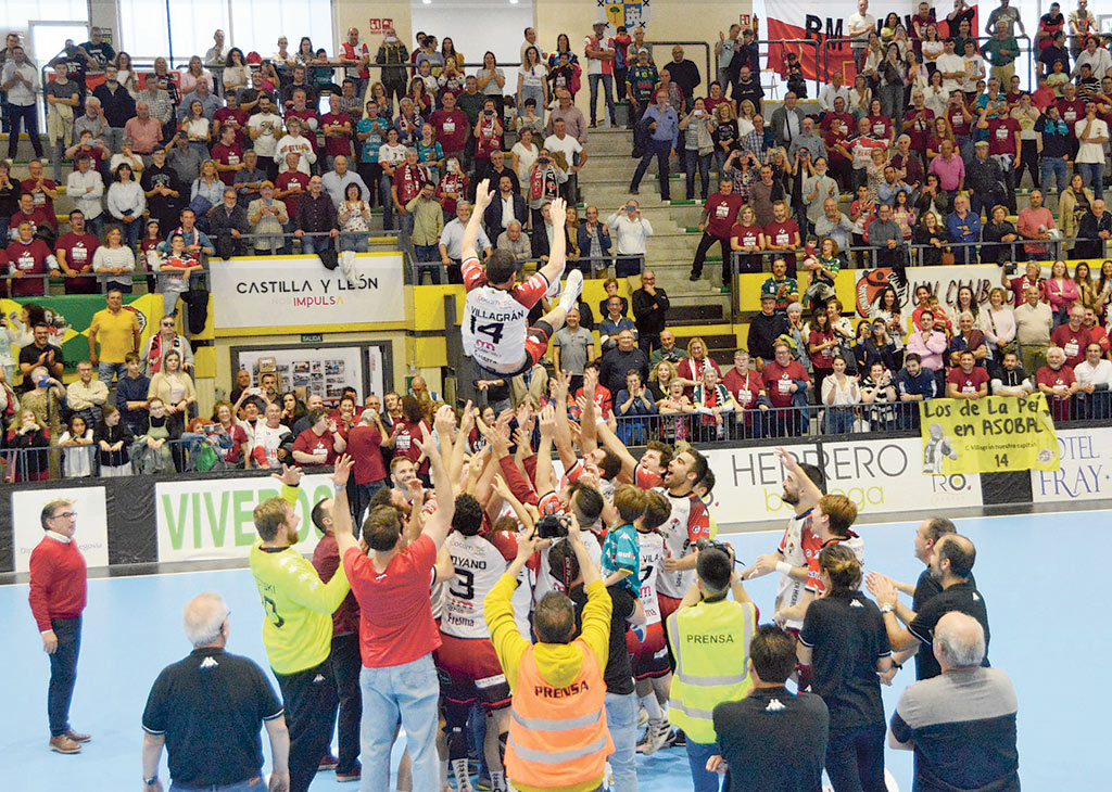 Los componentes del Balonmano Nava elevan varios metros del suelo a Carlos Villagrán en un ‘manteo’ sobre la pista del pabellón./ AMADOR MARUGÁN