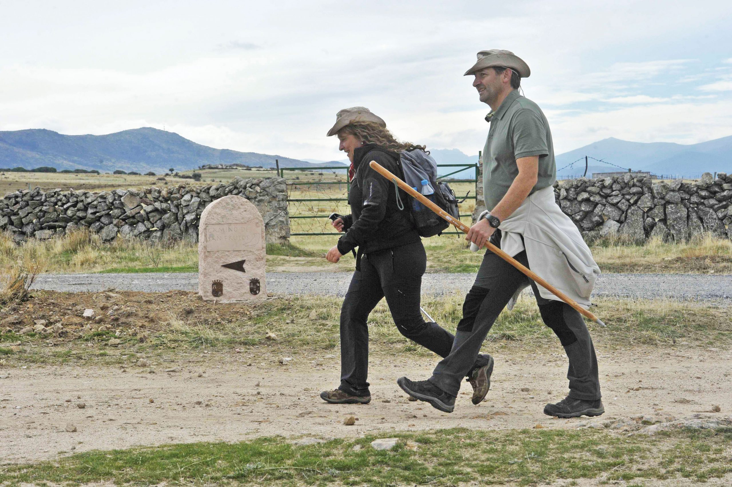 Dos peregrinos pasan caminando junto a uno de los mojones que indican el trayecto.