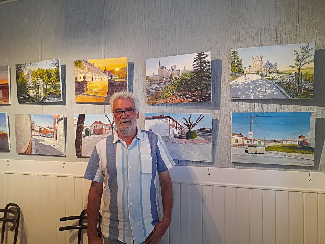 El pintor Miguel Ángel Maestro posa junto a parte de las obras que expone en el bar ‘Bulevar’ de Nava de la Asunción./ A. MARUGÁN