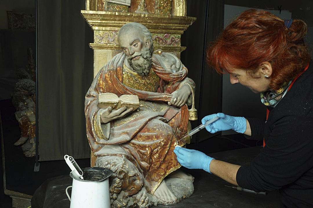 Una trabajadora fija el estrato pictórico de una figura en el Monasterio del Parral.