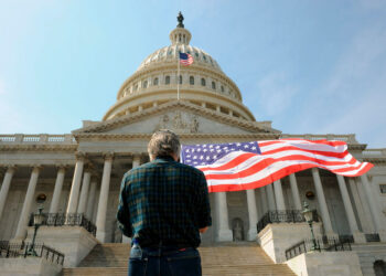 Un hombre con una bandera de los Estados Unidos delante del Capitolio en Washington.