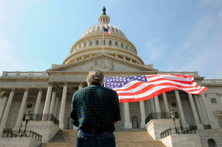Un hombre con una bandera de los Estados Unidos delante del Capitolio en Washington.